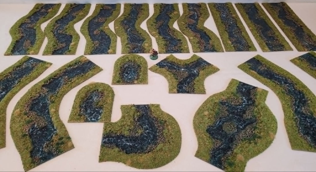 Handmade 28mm stream terrain set with 18 flocked river pieces including straights, bends, Y-fork junction, ponds, and spring ends, shown with miniature for scale